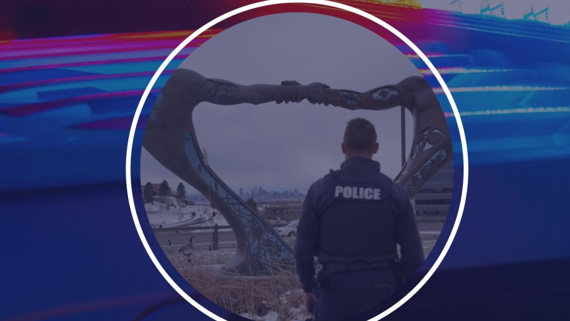 Police officer standing outside with a large statue in the background.