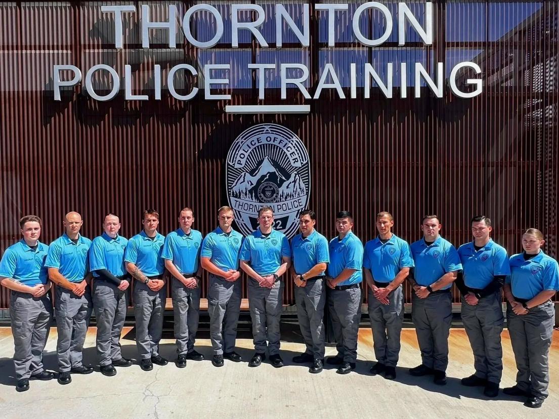 Police trainees in blue shirts stand in a line outside training facility.