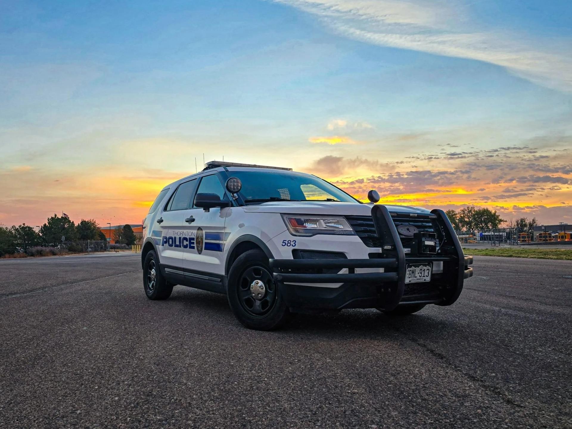 Police SUV parked on road at sunset, sky tinted with orange and blue.