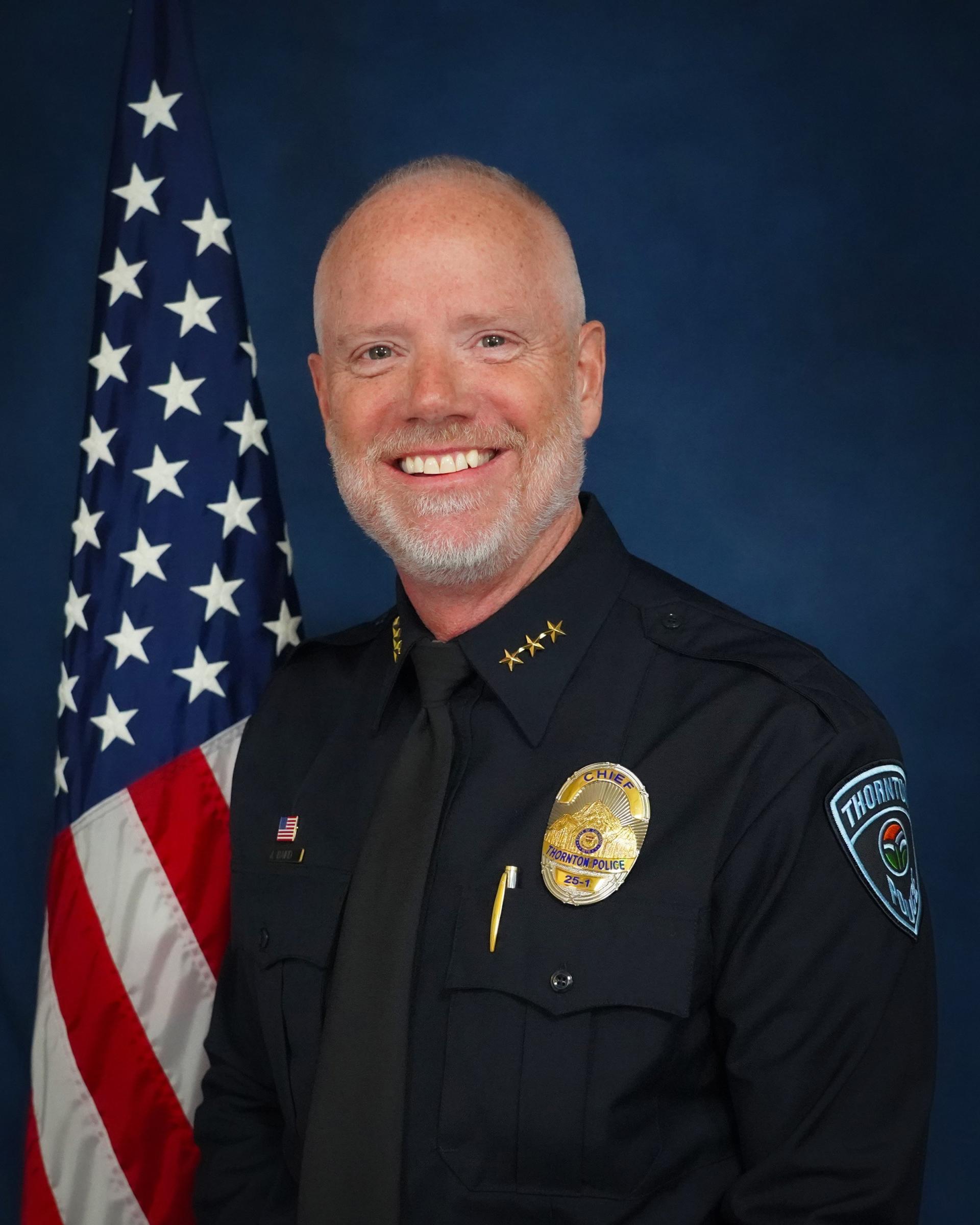 Smiling police officer in uniform with U.S. flag background.